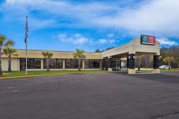 A hotel with a covered entrance, palm trees, and a clear blue sky. - Quality Inn Yemassee - Point South I-95 (Yemassee)