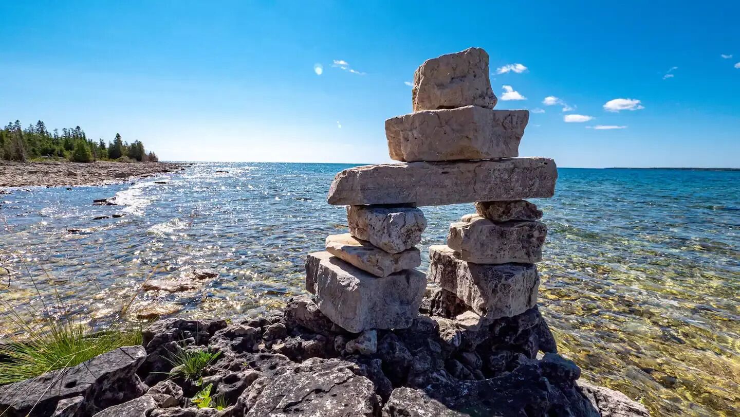 A stack of rocks by a clear lake with a distant shoreline.