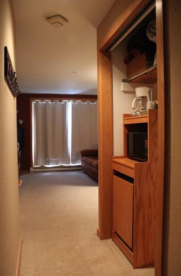 A compact living space with a kitchenette, a sofa, and a large window with curtains.
