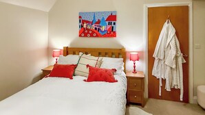 A bedroom with a bed, two bedside lamps, a painting on the wall, and a robe hanging on the door. - The Court House - UK43908 (Silloth)