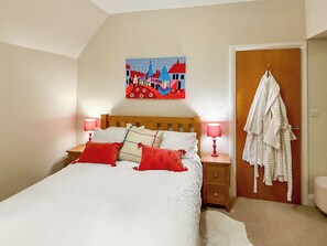 A bedroom with a bed, two bedside lamps, a painting on the wall, and a robe hanging on the door.