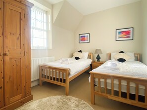 A bedroom with two wooden beds, a large wooden wardrobe, and a window with a view of buildings. - The Court House - UK43908 (Silloth)