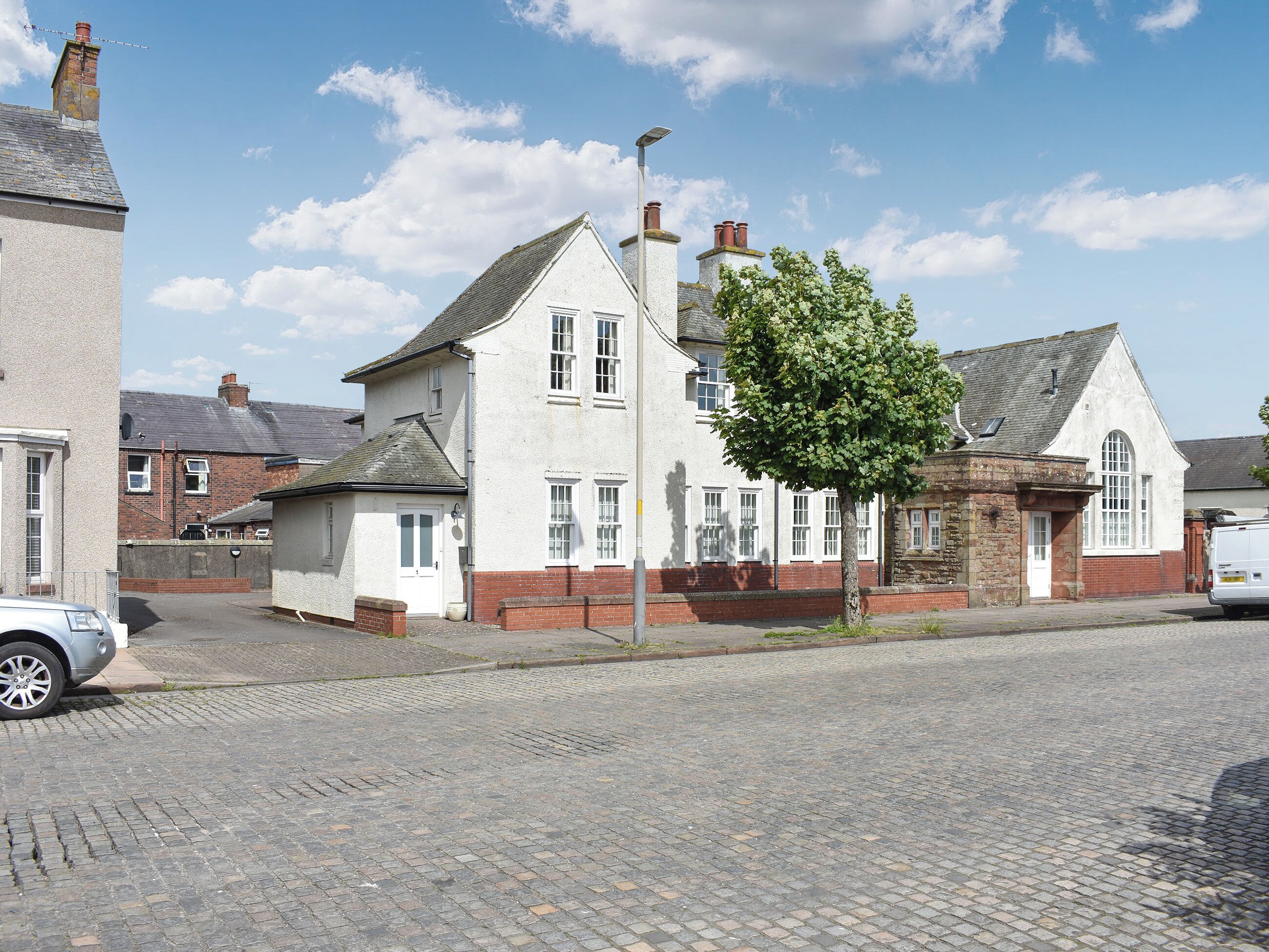 A traditional two-story house with a brick facade and white trim, a cobblestone driveway, and a tree in front.