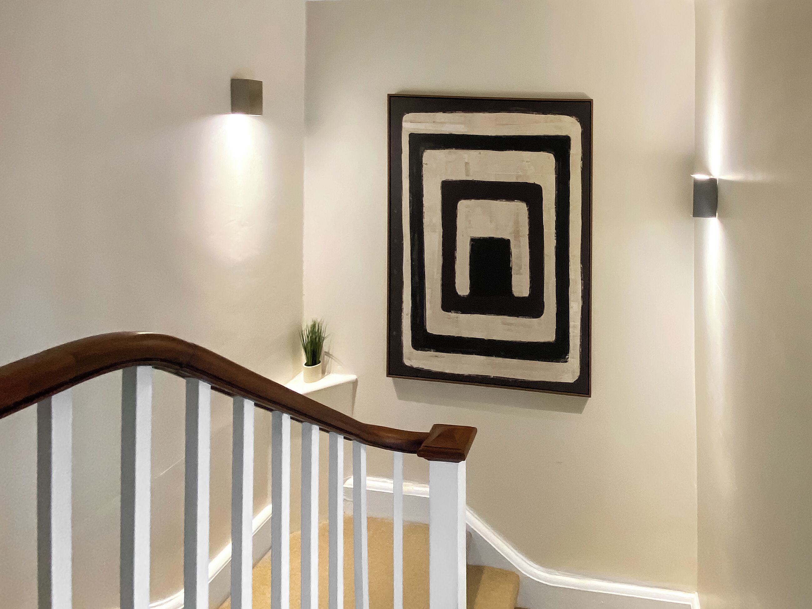 Una escalera con barandillas blancas y un pasamanos de madera que conduce a un rellano con un cuadro abstracto en blanco y negro en la pared.