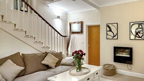 A living room with a staircase, a sofa, a coffee table with a vase of flowers, a television, and artwork on the wall. - The Court House - UK43908 (Silloth)