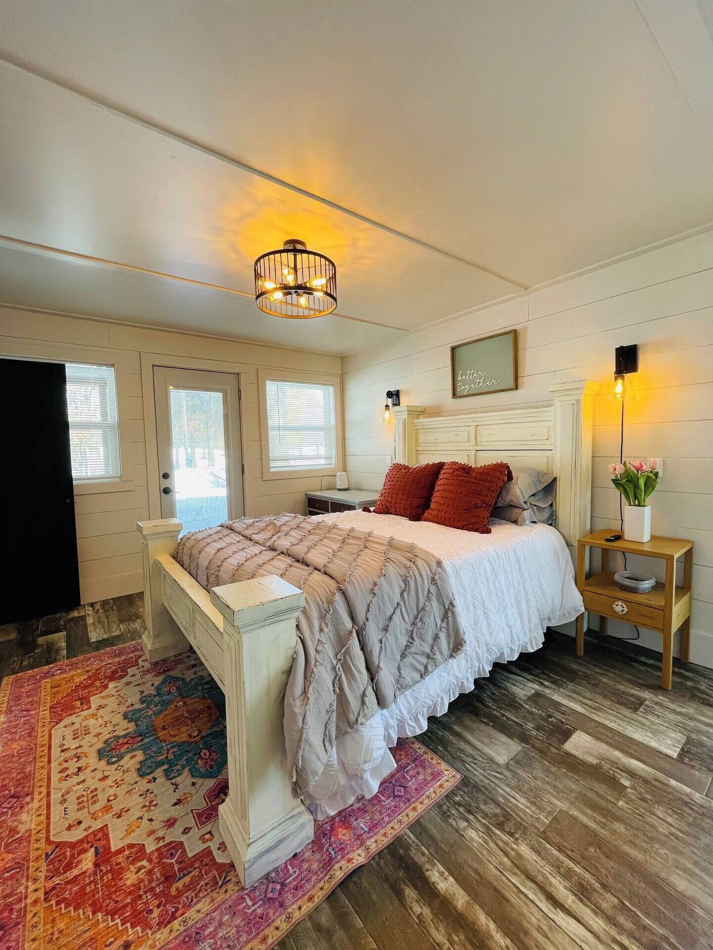 A bedroom with a bed, a nightstand, a lamp, a wall clock, and a window.
