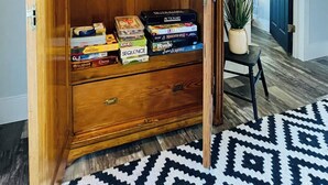 A wooden cabinet with books and games, a small table with a plant, and a patterned rug.