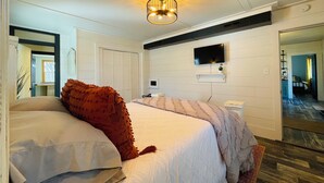 A bedroom with a bed, a television, a small shelf, and a door.