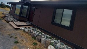Una casa moderna de un piso con fachada oscura, ventanas amplias y un camino de piedra que lleva a la entrada.