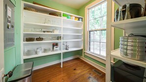 Une cuisine avec un plancher en bois, des étagères blanches et une fenêtre.