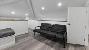 A small, modern room with a loft bed, a black sofa, and a white door. - AV Bungalows #9A with Loft (Arcadia)