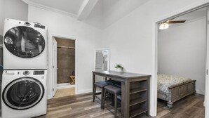 A laundry room with a front-loading washer and dryer, a small table with chairs, and a bed with a wooden headboard. - AV Bungalows #9A with Loft (Arcadia)