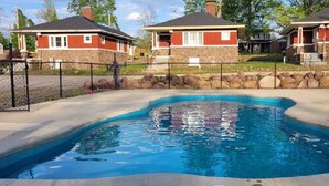 A swimming pool with a curved edge, surrounded by a stone wall and a fence. - AV   Bungalows    #8 (Arcadia)