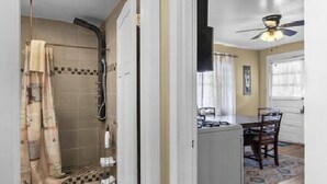 A hallway with a shower, a dining area with a table and chairs, and a ceiling fan. - AV   Bungalows    #8 (Arcadia)