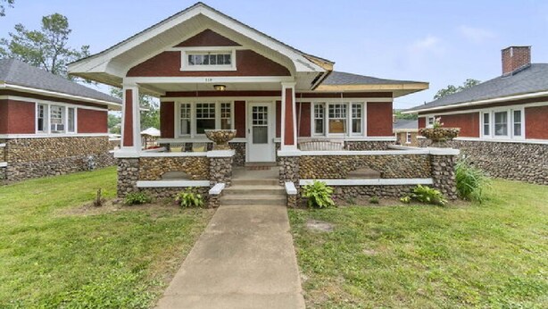 A two-story house with a stone foundation, a front porch, and a pathway leading to the entrance. - AV    Bungalows   #7 (Arcadia)