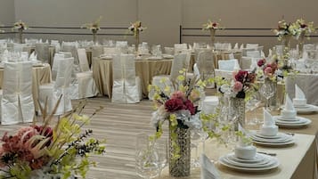 A banquet hall with tables set for a formal event, featuring white tablecloths, glassware, and floral centerpieces.
