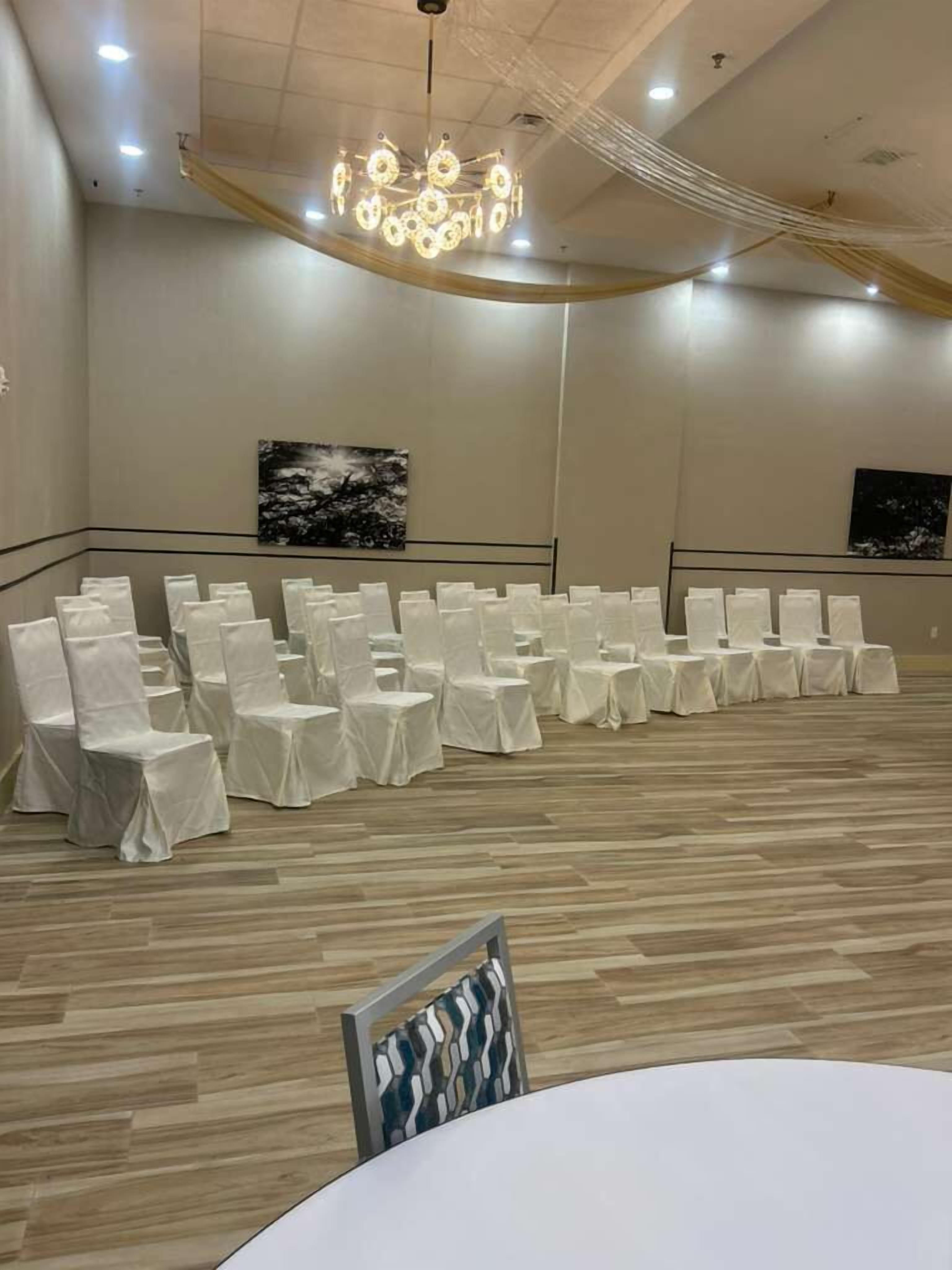 Un salón de conferencias con filas de sillas y mesas cubiertas de blanco, una araña y obras de arte en las paredes.