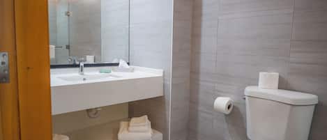 A modern bathroom with a white sink, mirror, and toilet. There is a towel rack and a shelf with folded towels.