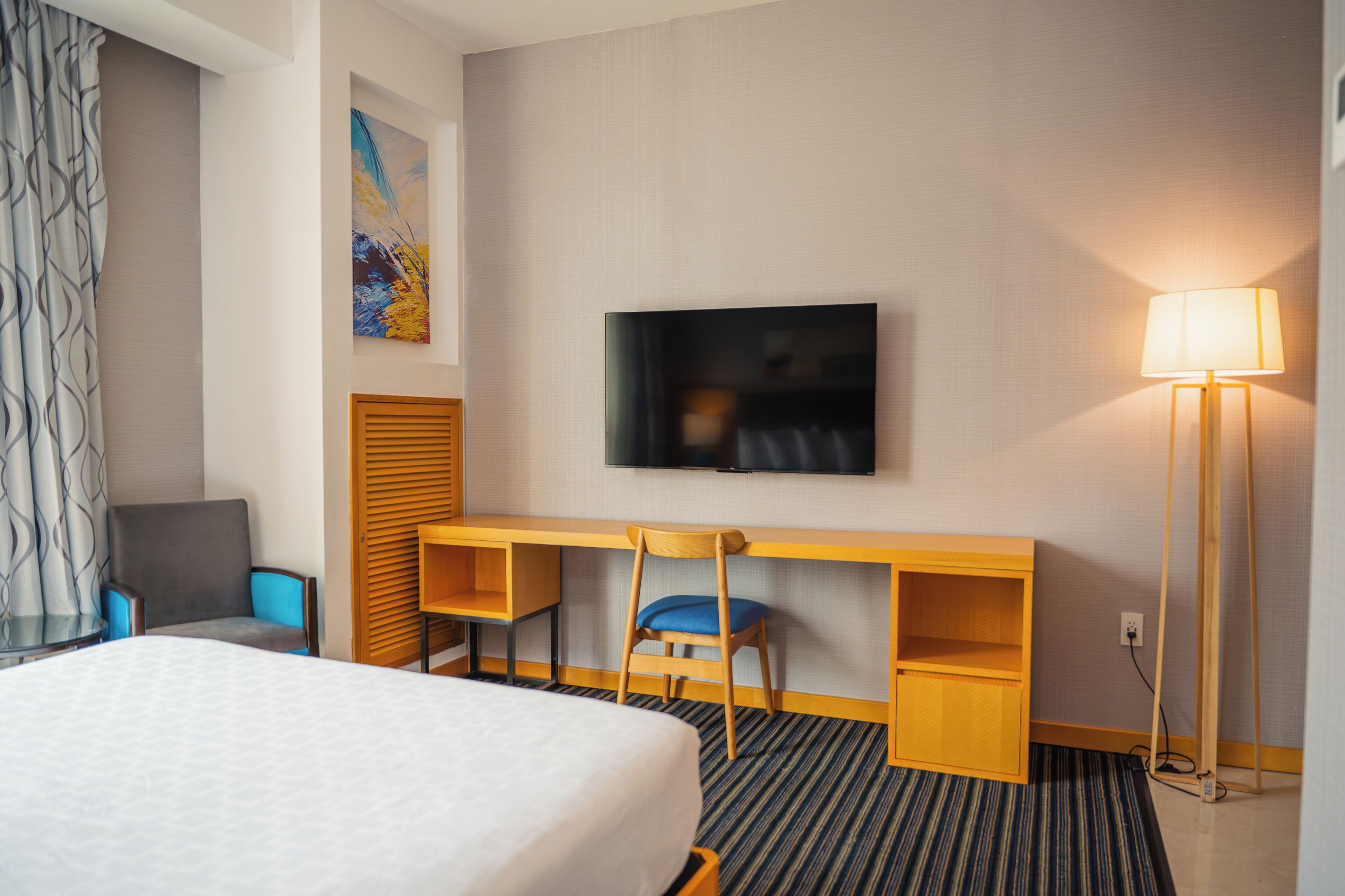 A hotel room with a bed, a desk with a chair, a television, and a lamp.
