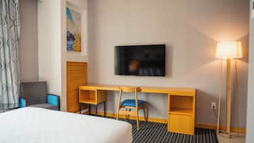 A hotel room with a bed, a desk with a chair, a television, and a lamp.