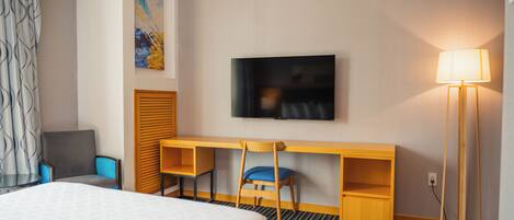 A hotel room with a bed, a desk with a chair, a television, and a lamp.