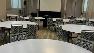 Ein Konferenzraum mit mehreren Tischen und Stühlen, einer Projektionsleinwand und einem Kronleuchter.