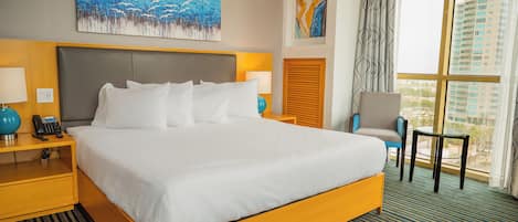 A hotel room with a large bed, bedside tables with lamps, a chair, and a view of buildings through the window.