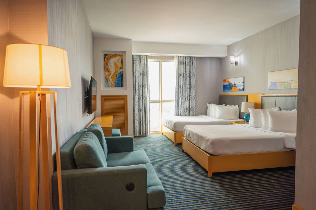 Habitación de hotel con dos camas, un sofá, un televisor y una ventana con cortinas.