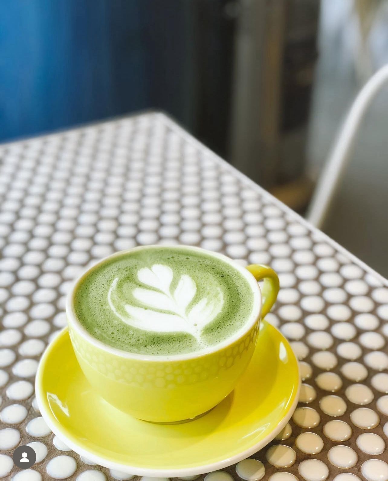A cup of green coffee with latte art on a yellow saucer, placed on a table with a polka dot pattern.