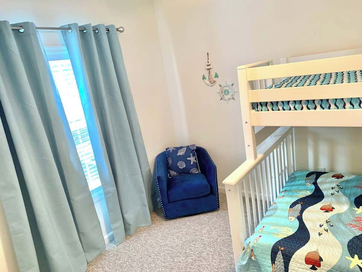 A room with a bunk bed, a blue chair, and a window with curtains.