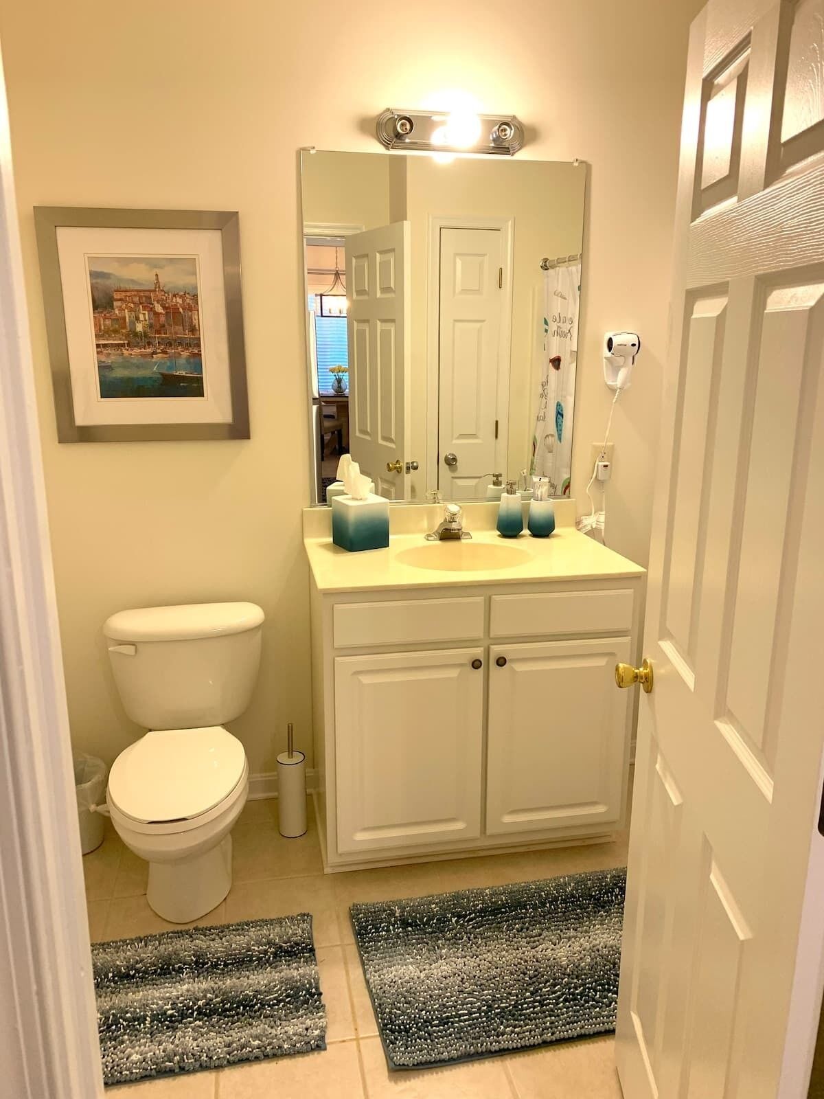 A bathroom with a toilet, sink, mirror, and framed picture on the wall.