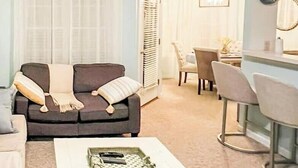 En stue med en mørk sofa, et hvidt sofabord og et spiseområde med bord og stole.
