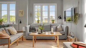 Ein gemütliches Zimmer mit einem gestreiften Sofa, einem Holztisch und einem an der Wand montierten Fernseher.