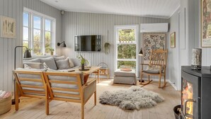 Ein gemütliches Wohnzimmer mit einer Holzsofa, einem Schaukelstuhl, einem Kamin und einem großen Fenster mit Blick auf Grünflächen.