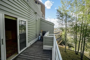 Un edificio residencial con terraza de madera, puertas corredizas de vidrio y vista a un área boscosa.