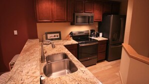 A compact kitchen with dark wooden cabinets, a stainless steel sink, a microwave, a stove, and a refrigerator.