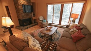 A cozy living room with a stone fireplace, a large window with a view, and a comfortable seating area.