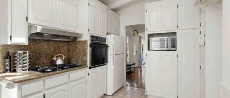 A kitchen with white cabinets, a gas stove, a stainless steel range hood, and a tiled floor.