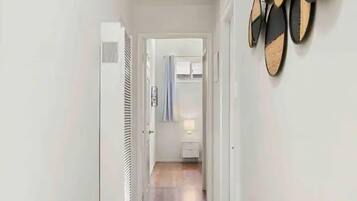 A narrow hallway with a tiled floor, a white radiator, and a door leading to a room with a shower.