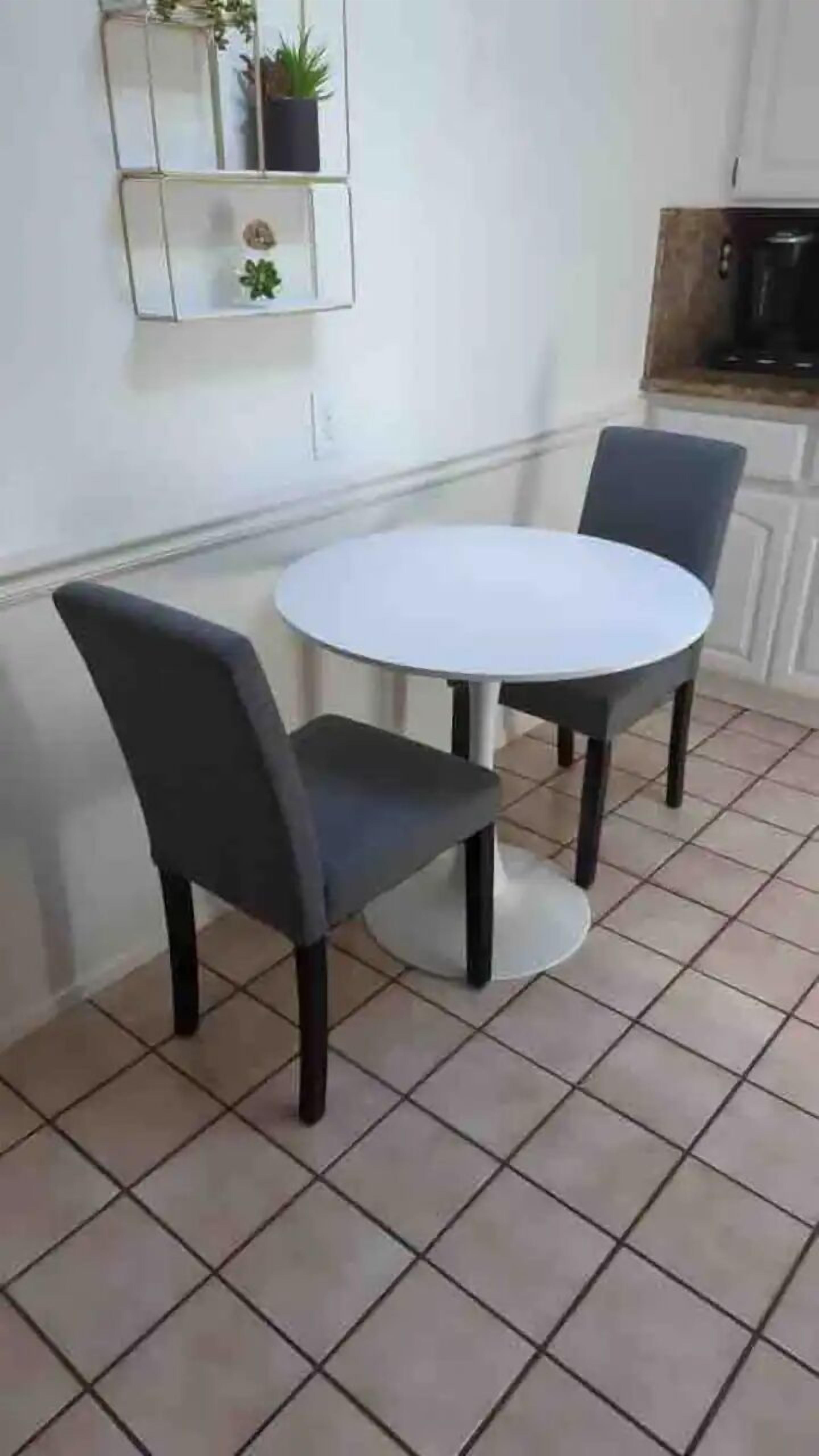 Un pequeño comedor con una mesa redonda y dos sillas. Encima de la mesa, una estantería con plantas.