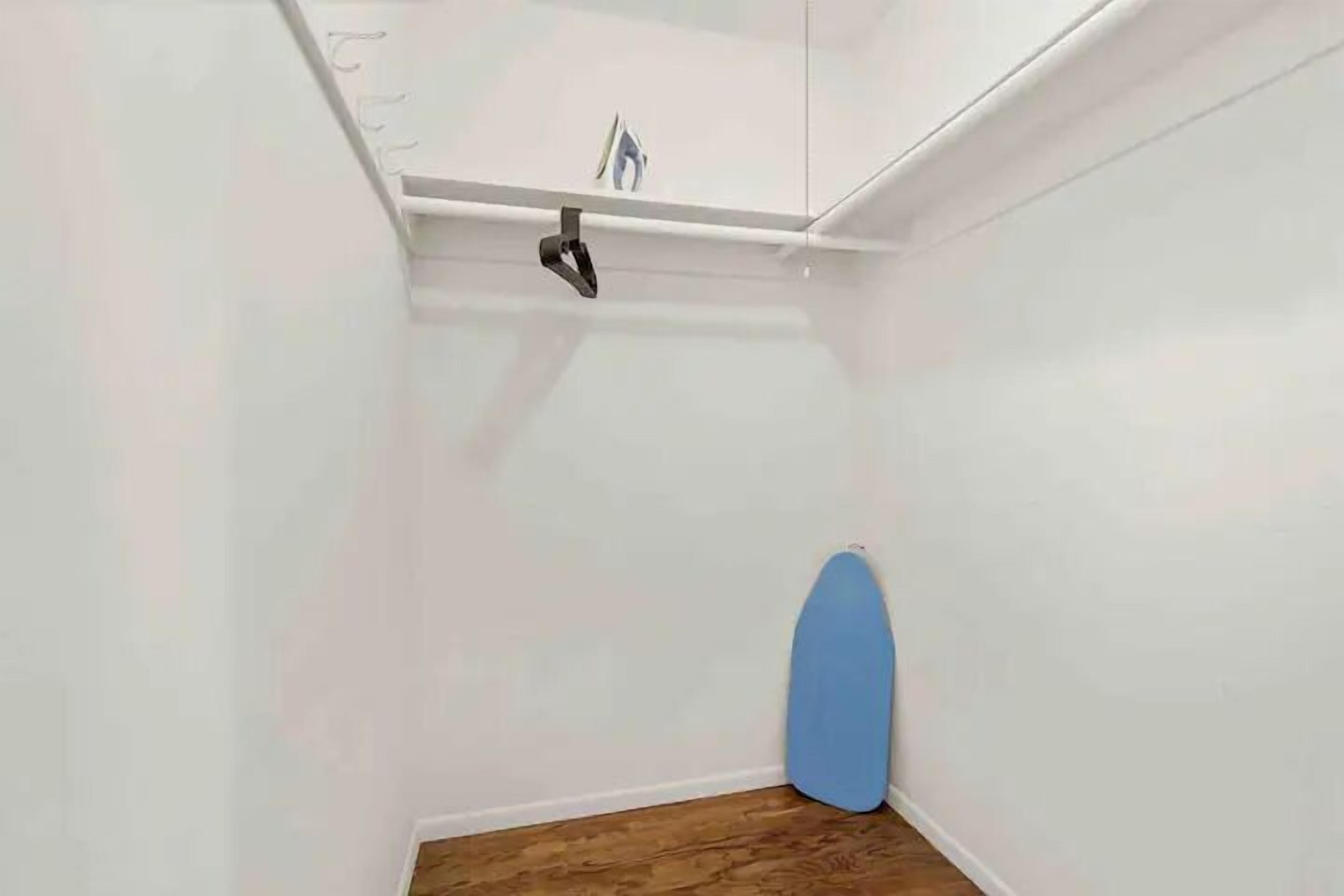 Una habitación pequeña con piso de madera, pared blanca y un objeto azul apoyado contra la pared.