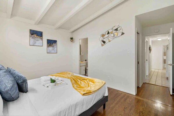 A bedroom with a bed, pillows, a bedside table, a mirror, and a wall art piece. - Mid Century Garden View Home Parking (San Mateo)