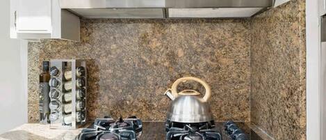 Une cuisine équipée d’une hotte en acier inoxydable, d’un plan de travail en granit et d’une bouilloire posée sur la cuisinière.