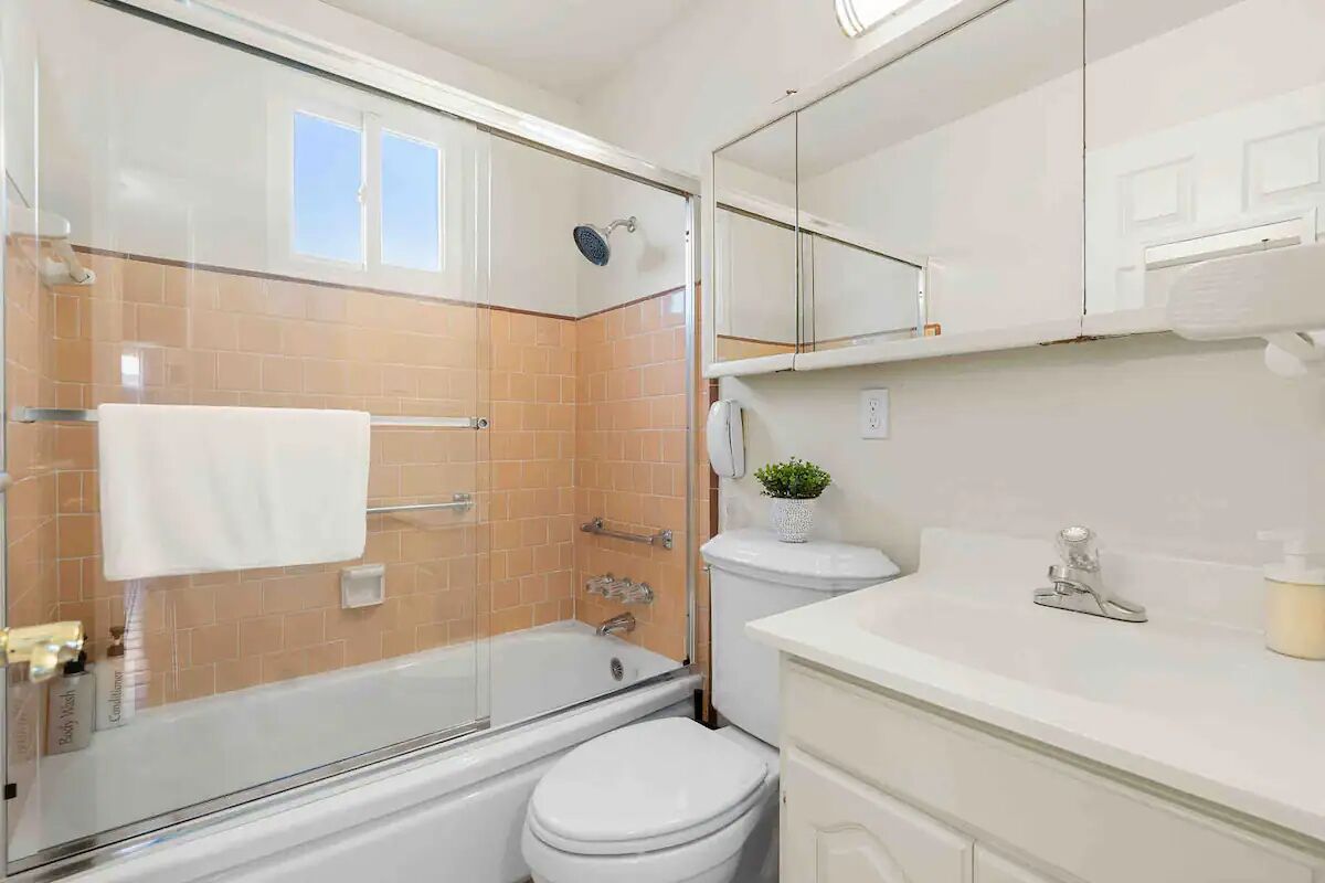 A modern bathroom with a glass-enclosed shower, a white toilet, and a sink with a mirror above.