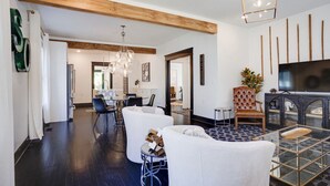 Un salon moderne avec un grand téléviseur, un plafond en bois et un coin repas à l’arrière-plan.