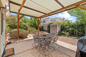 A covered patio with a round metal table and chairs, surrounded by a brick patio and greenery. - Location! Location! Amazing *Hidden Gem* -NE Heights! Family and pet friendly 🐶  (Albuquerque)