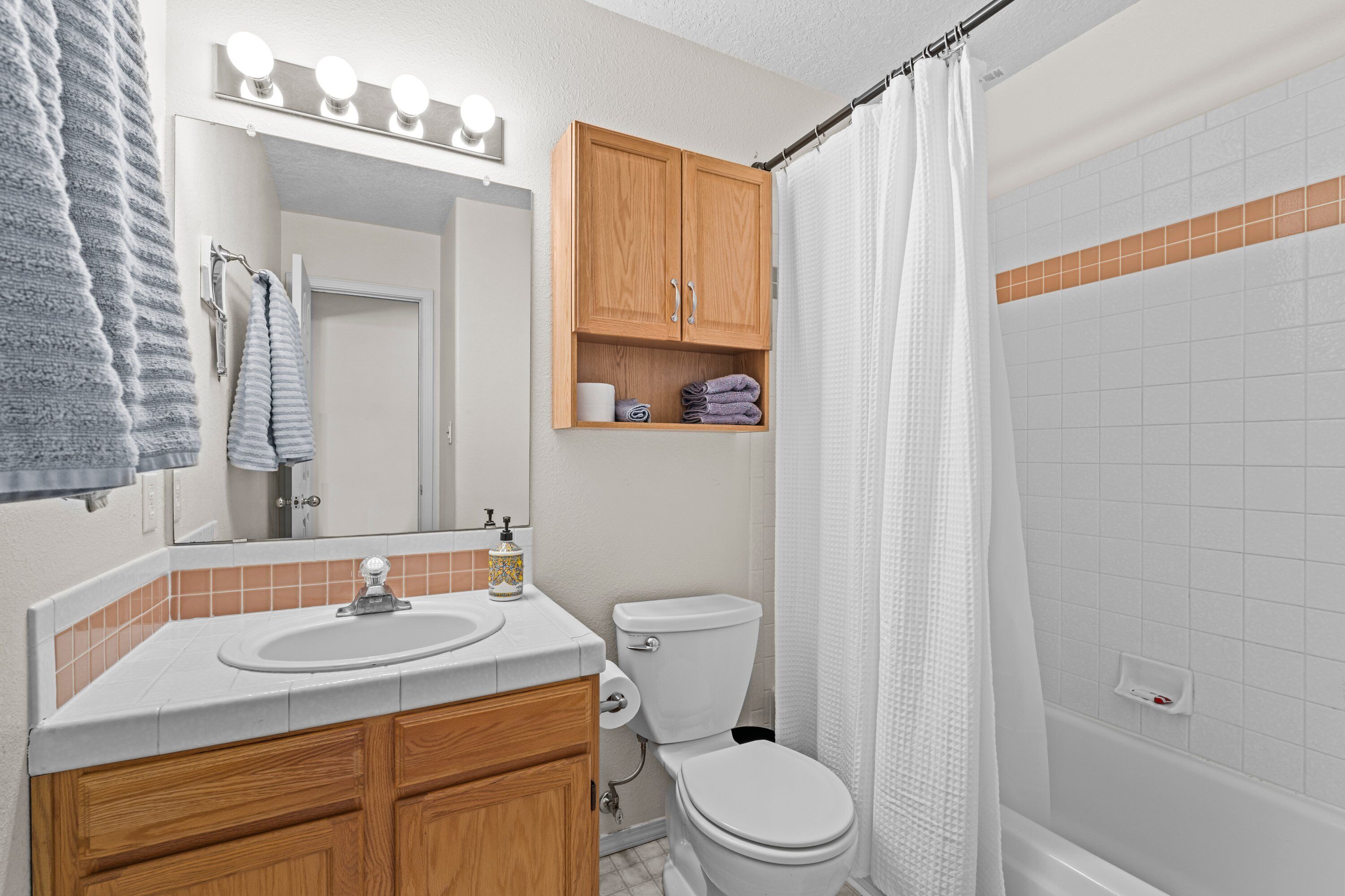 A bathroom with a sink, mirror, wooden cabinets, a toilet, and a shower area.