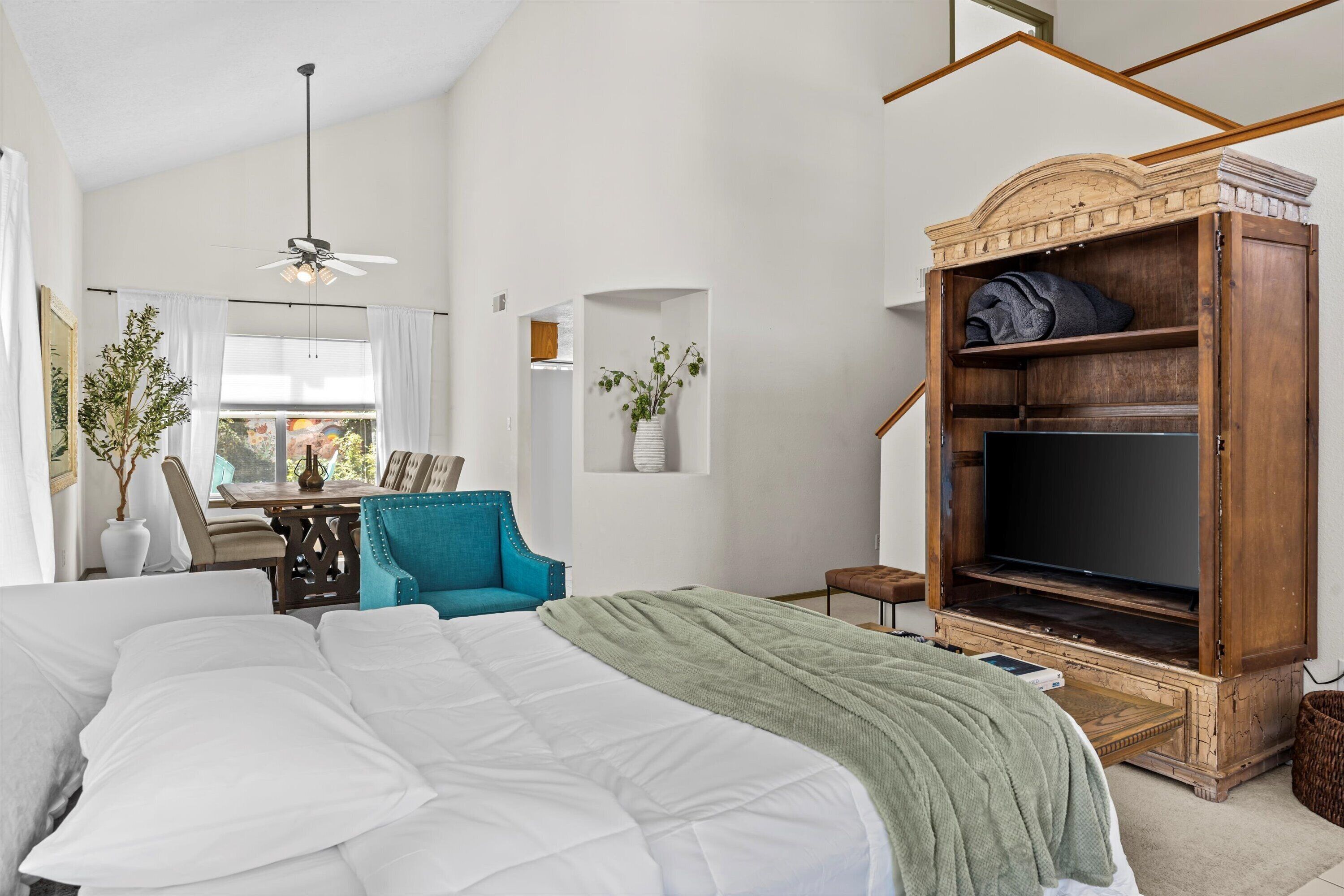 Ein Schlafzimmer mit einem Bett, einem Schreibtisch, einem Sessel, einem TV-Schrank und einem Deckenventilator.