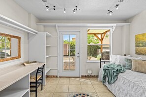 A bedroom with a bed, a desk, and a chair. There is a door leading to a patio area with a view of greenery. - Location! Location! Amazing *Hidden Gem* -NE Heights! Family and pet friendly 🐶  (Albuquerque)
