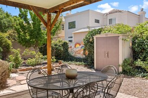 A patio with a round metal table and chairs, surrounded by a garden with a decorative wall and a shed. - Location! Location! Amazing *Hidden Gem* -NE Heights! Family and pet friendly 🐶  (Albuquerque)